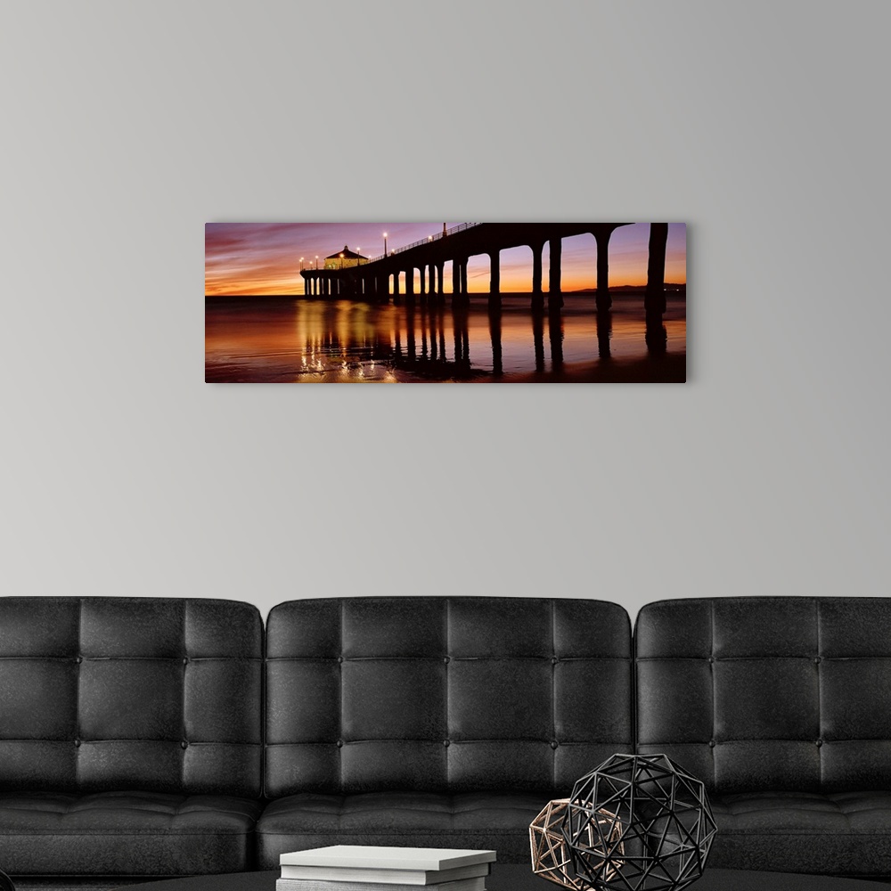 A modern room featuring A panoramic photograph of the silhouette of a long pier over the ocean at sunset.