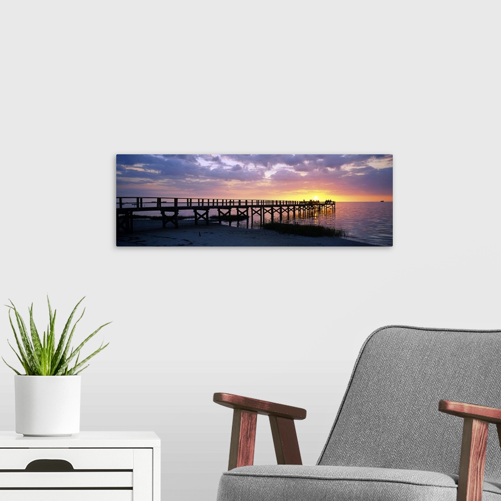 A modern room featuring Oversized, panoramic photograph of the pier extending into the water, toward the setting sun at C...