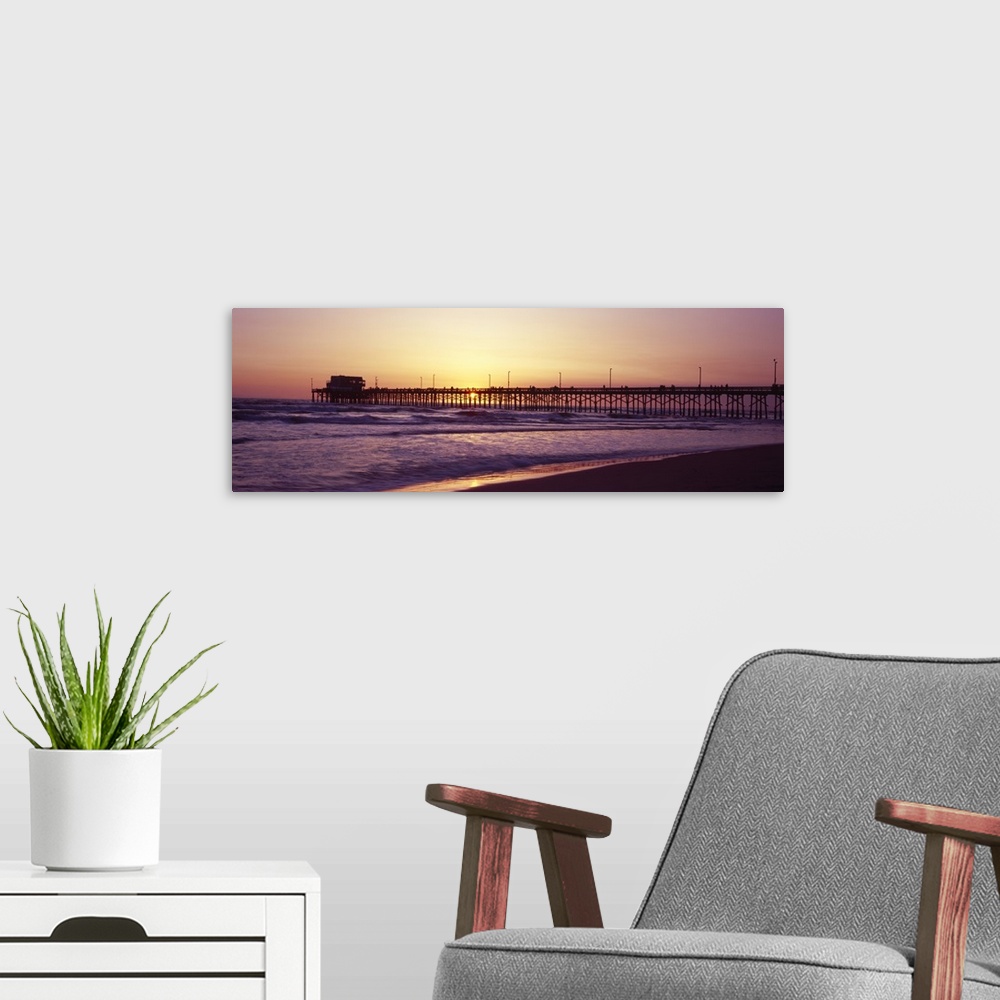 A modern room featuring Panoramic photograph of the sunset that can barely be seen behind a long pier that reaches far ou...