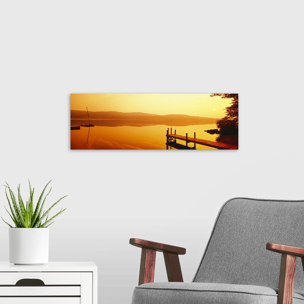 A modern room featuring A dock and boat reflect on these still waters at sunrise in this panoramic photograph wall art.