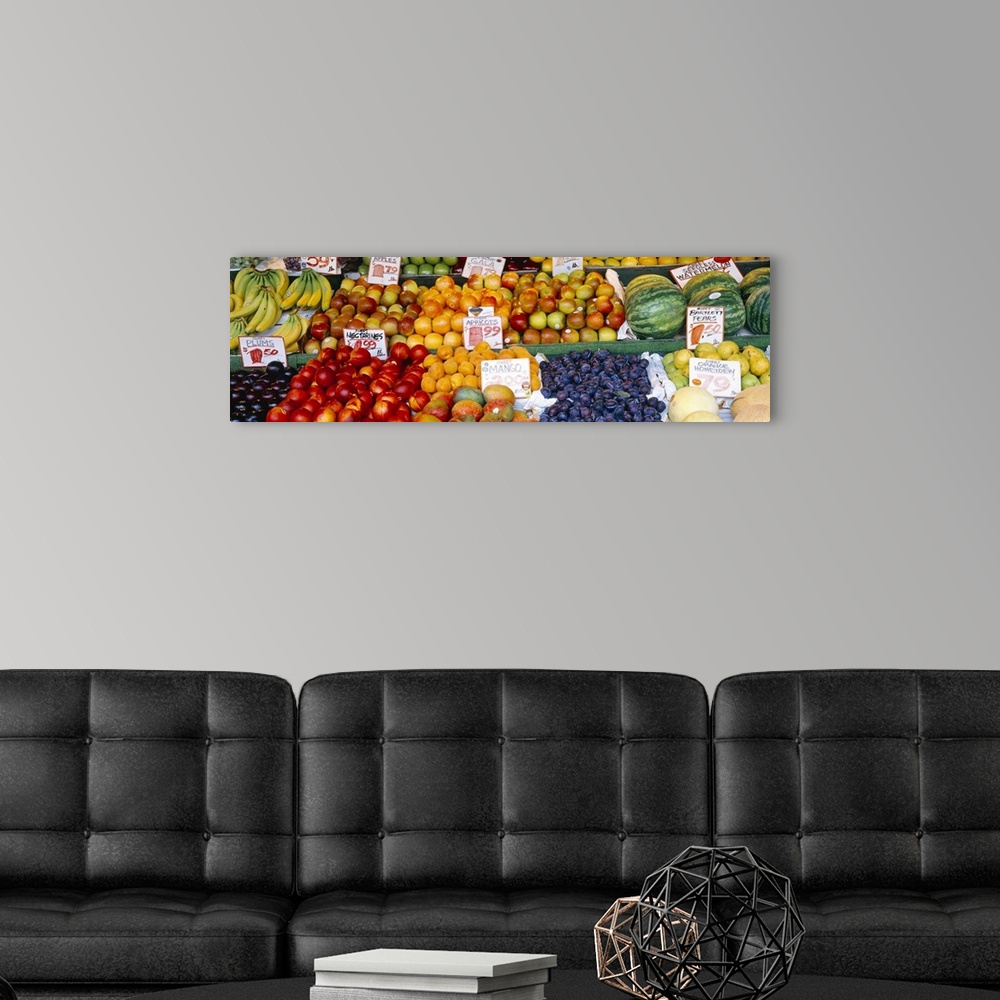 A modern room featuring Large, horizontal photograph of a fruit stand with many types of fruit and pricing signage in eac...