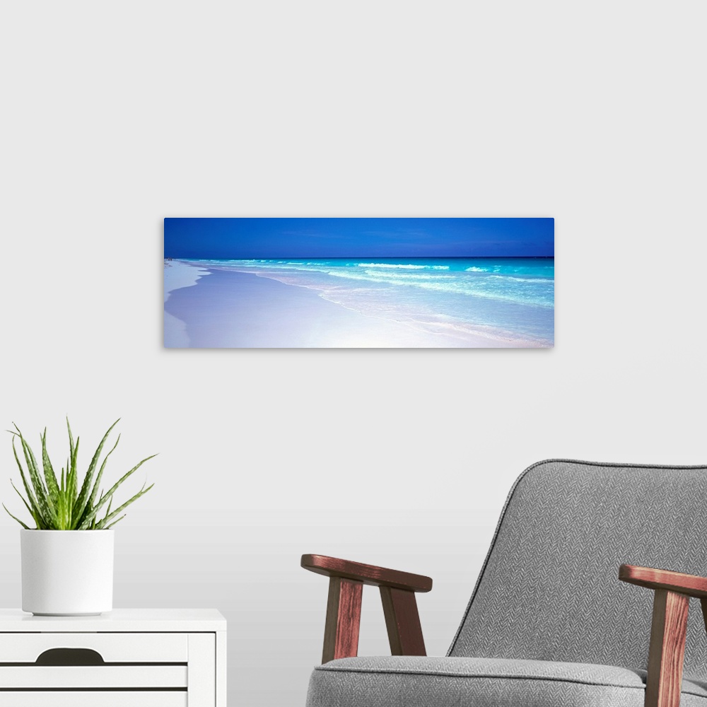 A modern room featuring A panoramic wall art picture of a tropical beach with flawless sand and a clear horizon as waves ...