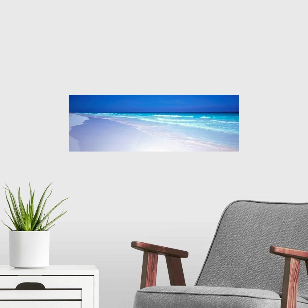 A modern room featuring A panoramic wall art picture of a tropical beach with flawless sand and a clear horizon as waves ...