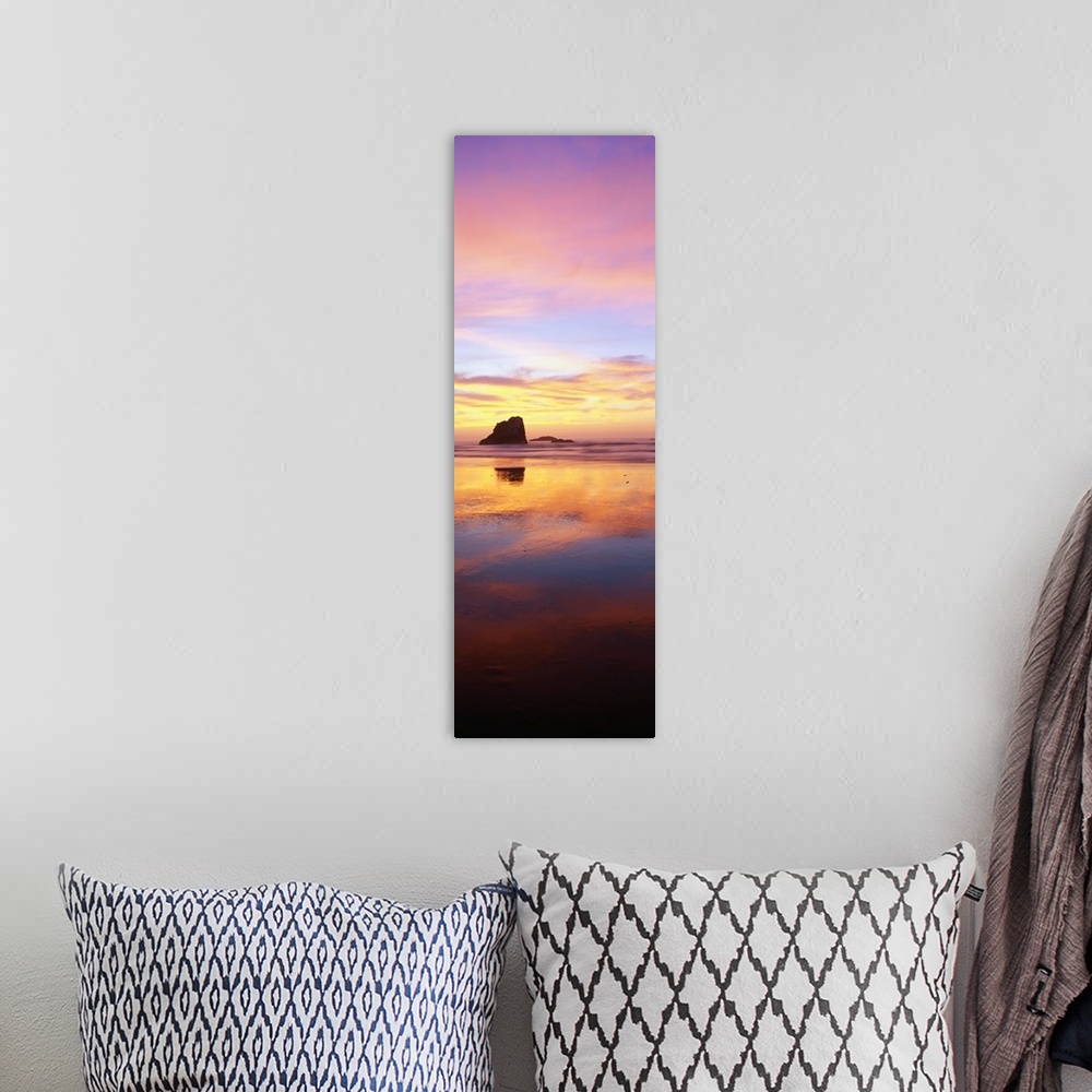 A bohemian room featuring A tall panoramic photograph is taken of a large rock formation in the ocean that is silhouetted i...