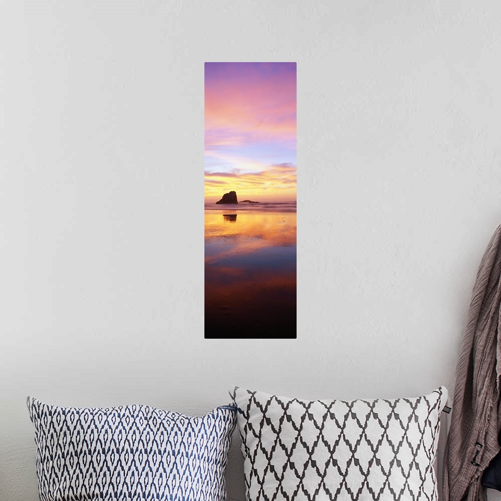 A bohemian room featuring A tall panoramic photograph is taken of a large rock formation in the ocean that is silhouetted i...