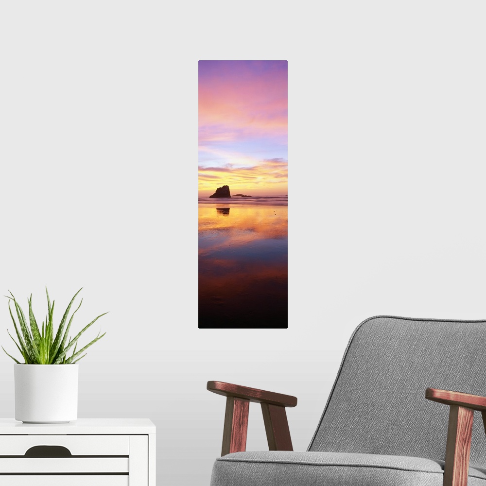 A modern room featuring A tall panoramic photograph is taken of a large rock formation in the ocean that is silhouetted i...