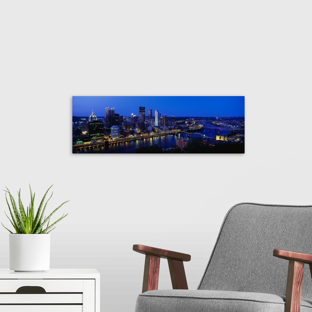 A modern room featuring This huge panoramic photograph is of the Pittsburg skyline at night with the buildings lit up and...