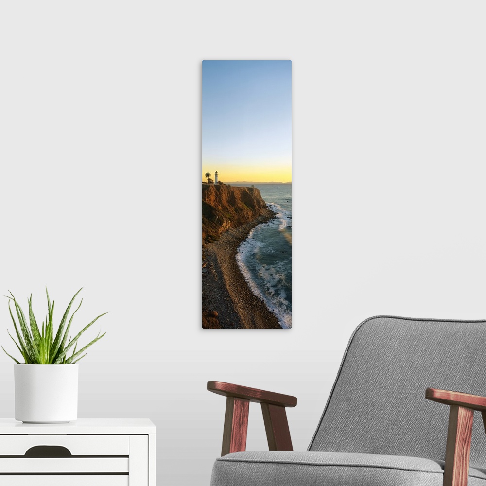 A modern room featuring Vertical panoramic canvas of a lighthouse sitting on a cliff near the ocean at sunset.