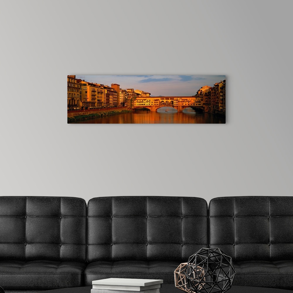 A modern room featuring Wide angle photograph of buildings alongside the Arno River, with a view of he Ponte Vecchio brid...