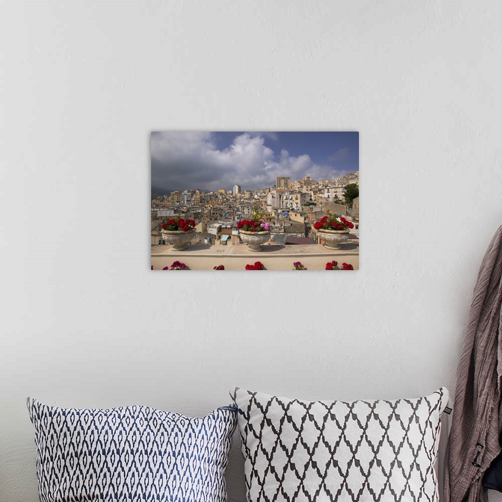A bohemian room featuring Canvas photo print of three flowers planted in pots along a balcony with an Italian city in the d...