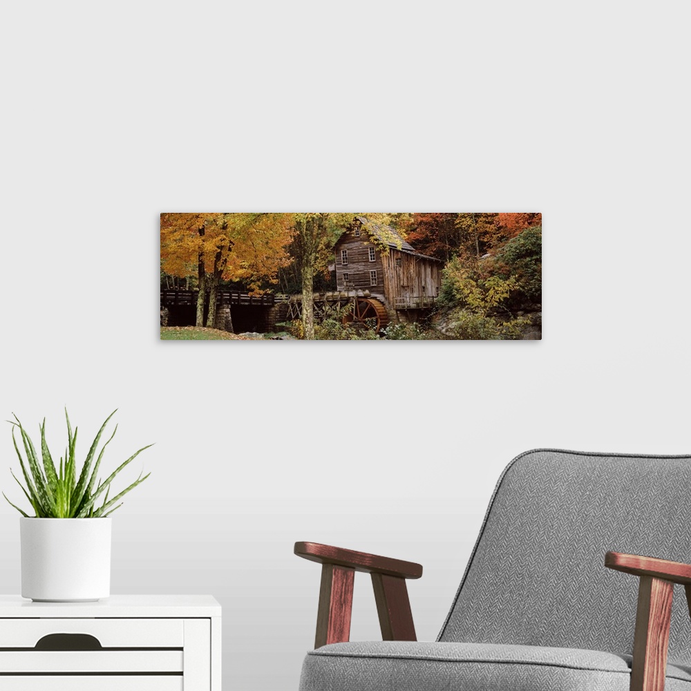 A modern room featuring Wide angle view of an old mill surrounded by trees and foliage in the autumn. A small bridge is s...