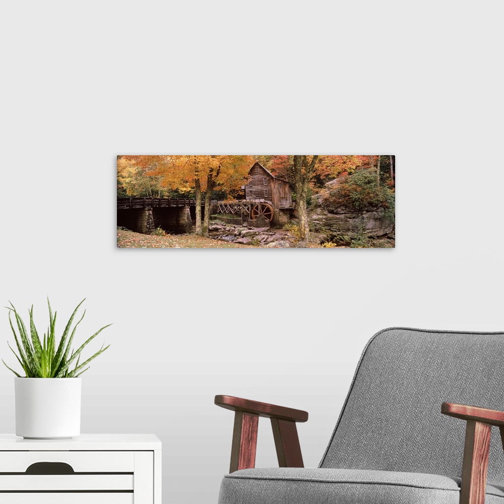 A modern room featuring Panoramic photograph of old stone bridge leading to water mill located in a fall forest.