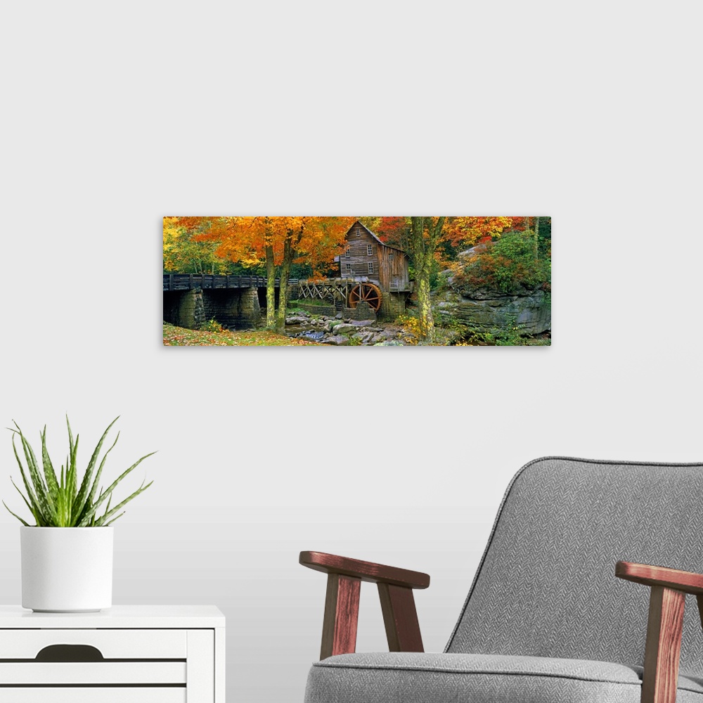 A modern room featuring Panoramic picture taken of a mill through autumn colored trees with a bridge just to the left.