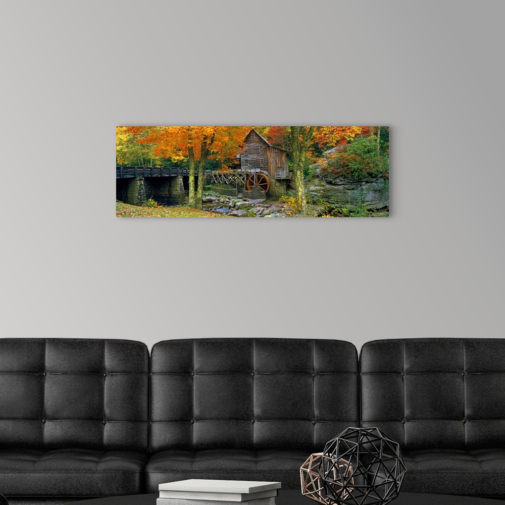 A modern room featuring Panoramic picture taken of a mill through autumn colored trees with a bridge just to the left.