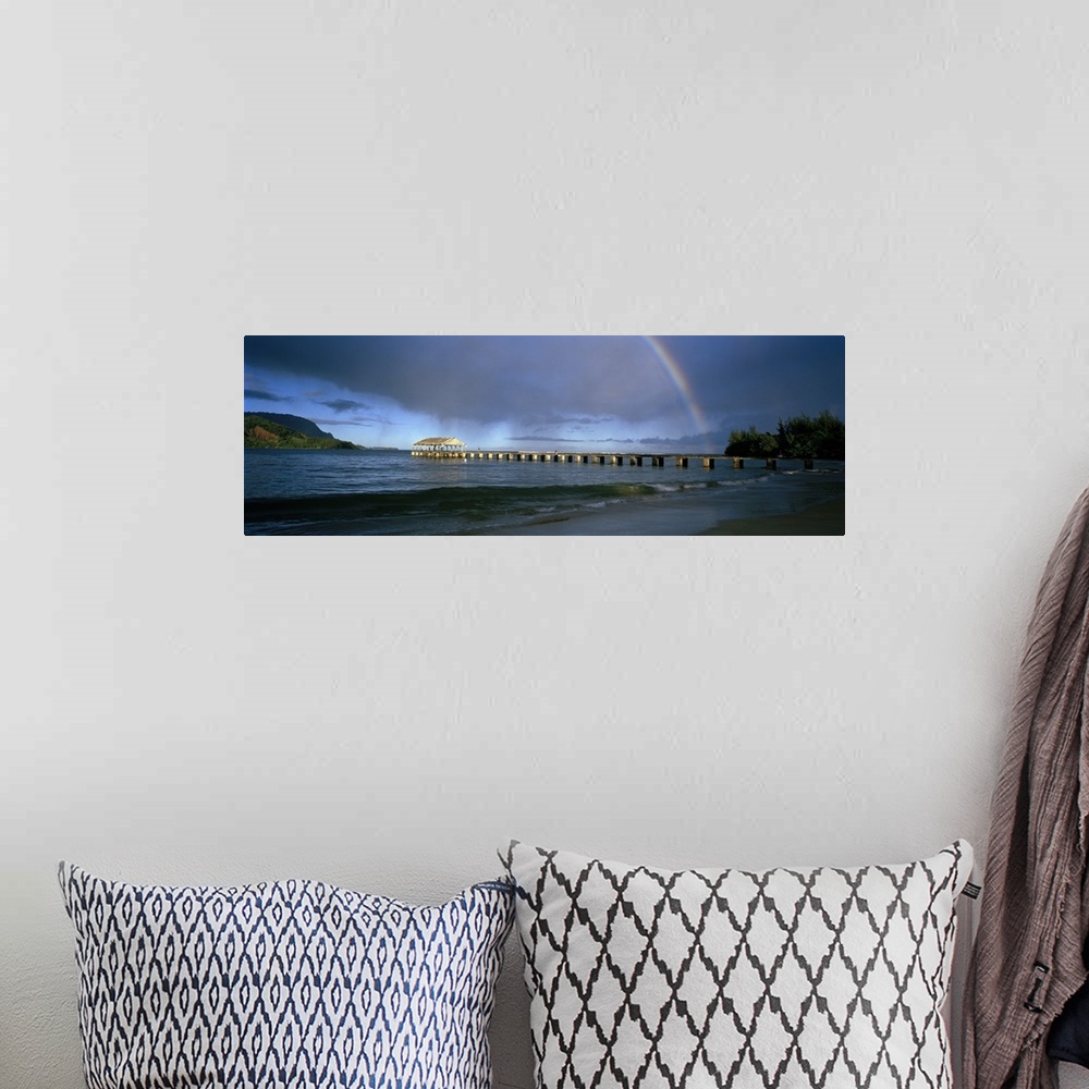 A bohemian room featuring Panoramic photograph of long dock stretching into ocean with rainbow overhead.  There are mountai...
