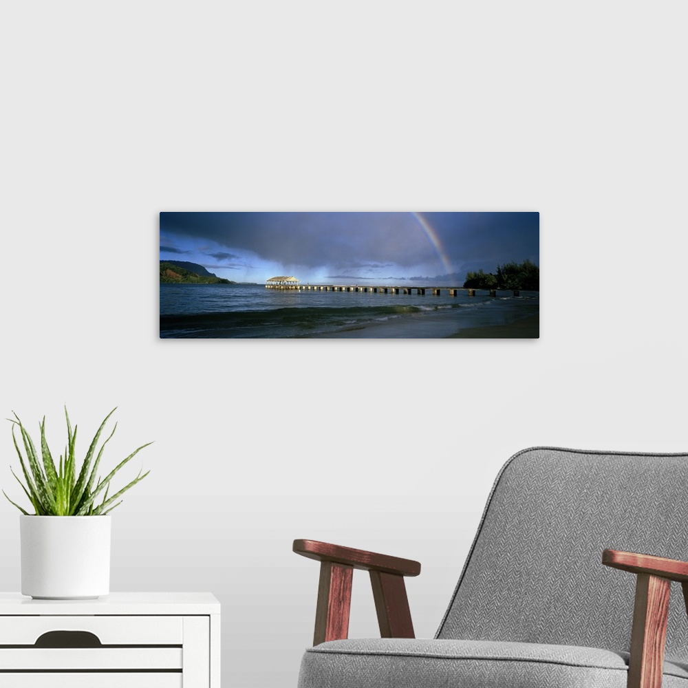 A modern room featuring Panoramic photograph of long dock stretching into ocean with rainbow overhead.  There are mountai...