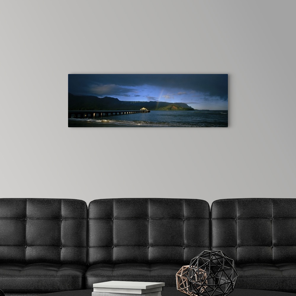 A modern room featuring Picture taken of a long pier that reaches far out into the ocean with a faint rainbow shown near ...
