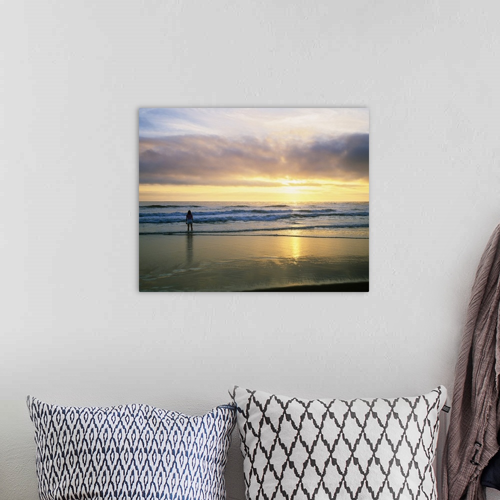 A bohemian room featuring In this landscape photograph a lone figure stands in the waves on the shore watching the sunset o...