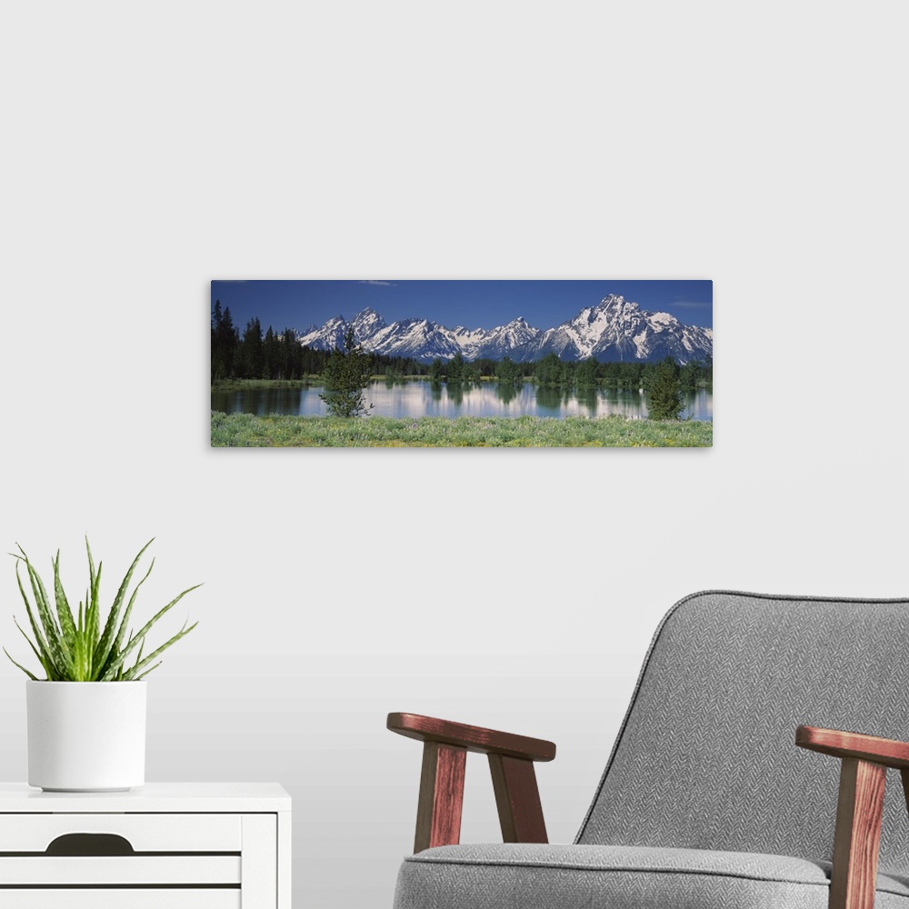 A modern room featuring Long canvas of snow capped mountains in the back of a forest reflected onto the waterfront.