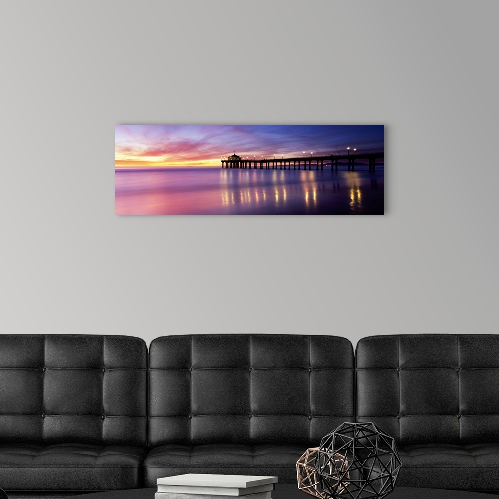 A modern room featuring Panoramic photograph of pier extending into ocean at sunset. The lights on the pier are reflected...