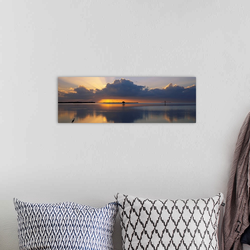 A bohemian room featuring Panoramic photograph of huge dark clouds reflected in water below at sunrise.  There is a small l...