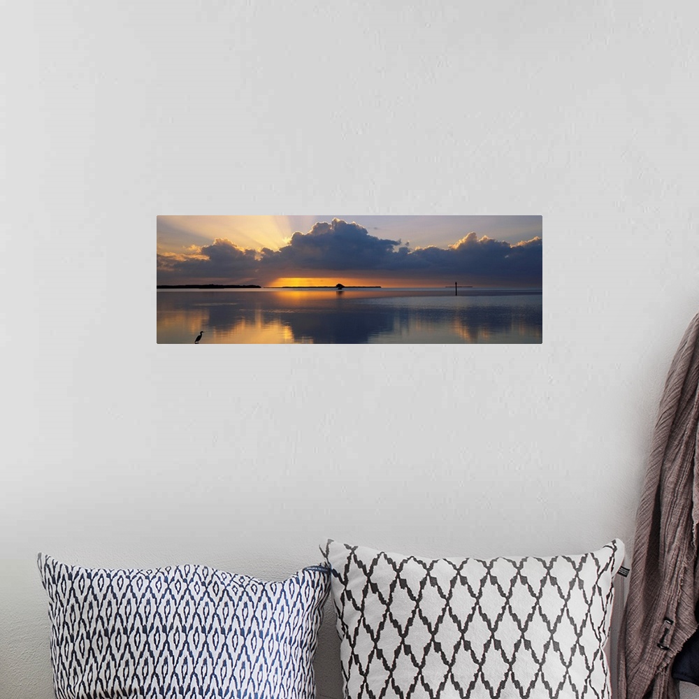 A bohemian room featuring Panoramic photograph of huge dark clouds reflected in water below at sunrise.  There is a small l...