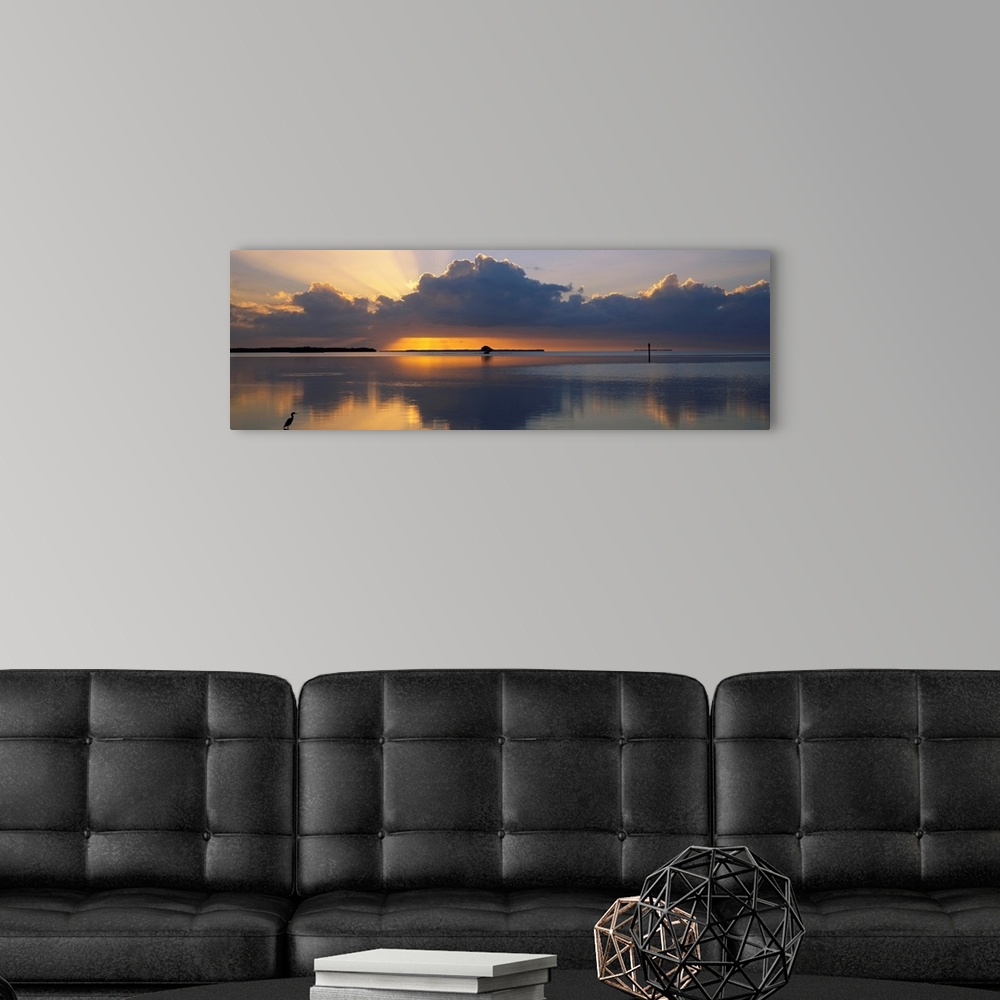 A modern room featuring Panoramic photograph of huge dark clouds reflected in water below at sunrise.  There is a small l...