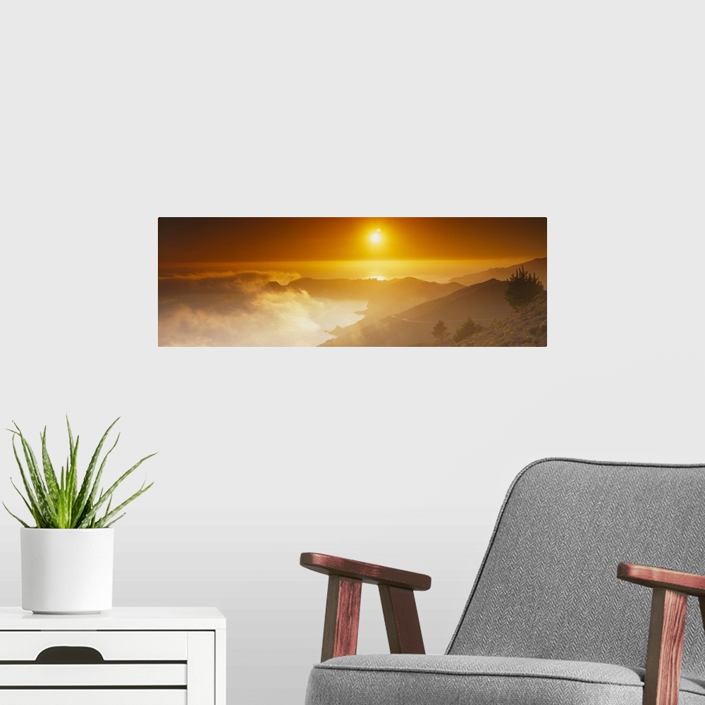 A modern room featuring Panoramic photo on canvas of the sun shining bright in the sky above an ocean and mountains with ...