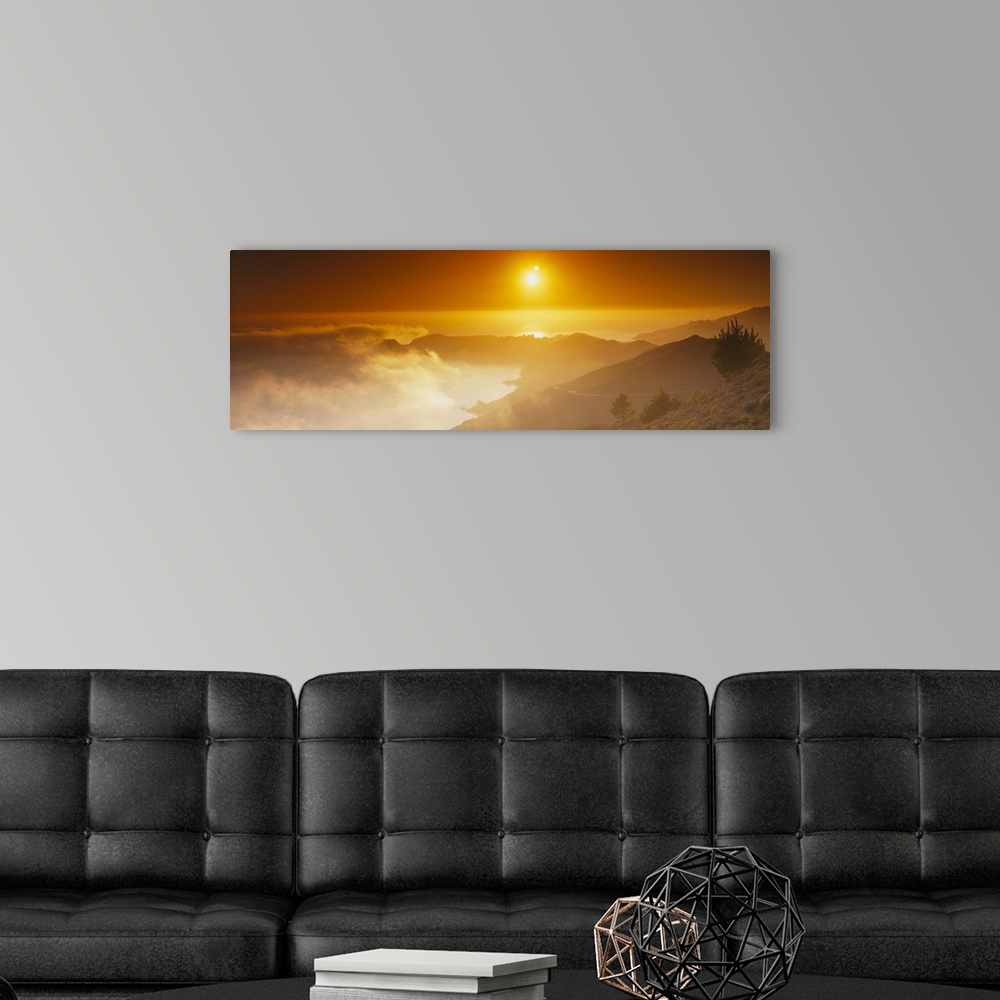 A modern room featuring Panoramic photo on canvas of the sun shining bright in the sky above an ocean and mountains with ...