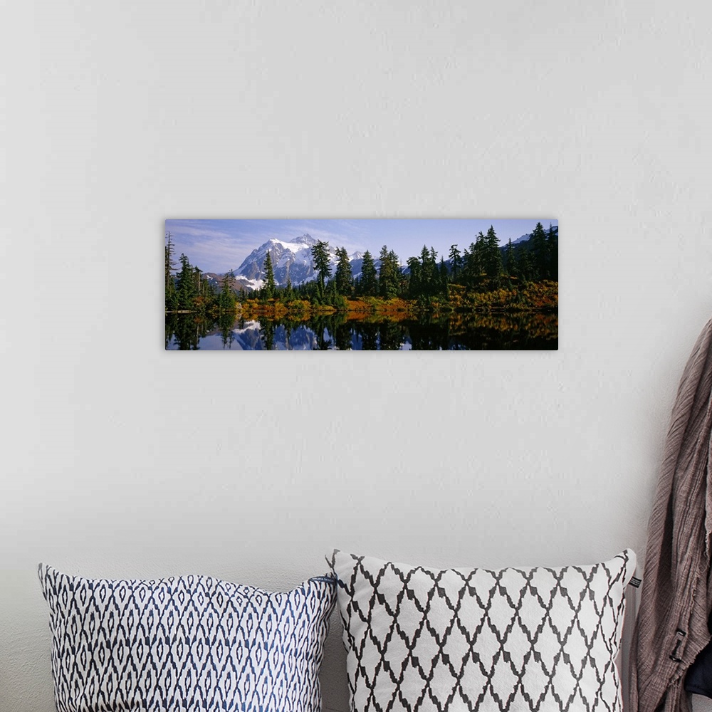 A bohemian room featuring Pine trees and a snow covered mountain reflect perfectly into the lake that sits in front of them.