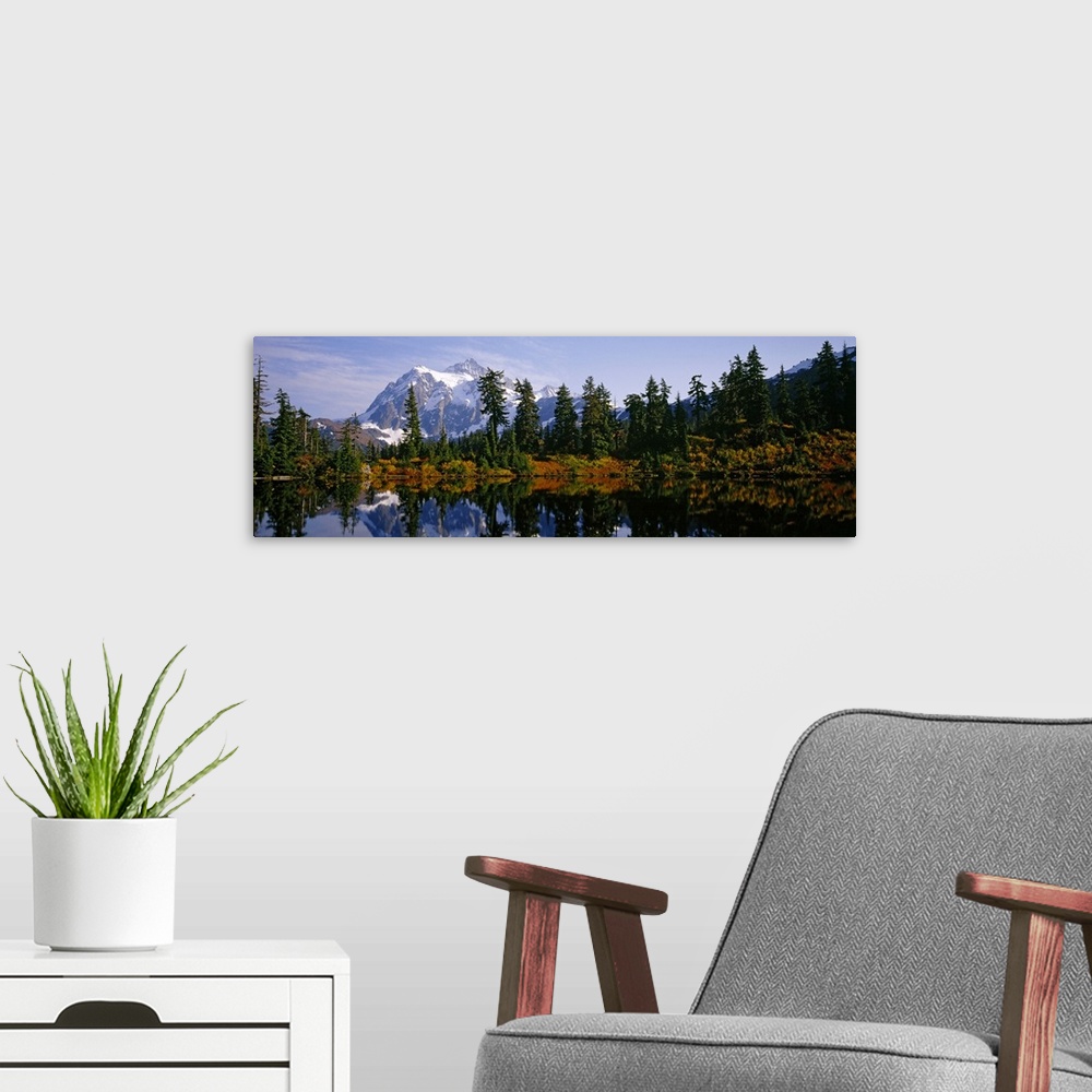 A modern room featuring Pine trees and a snow covered mountain reflect perfectly into the lake that sits in front of them.