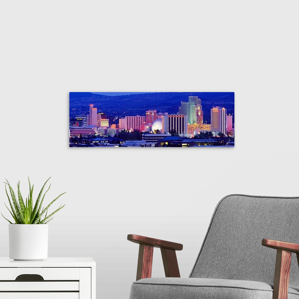 A modern room featuring The skyline in Reno is illuminated under a dark sky and photographed in panoramic view.
