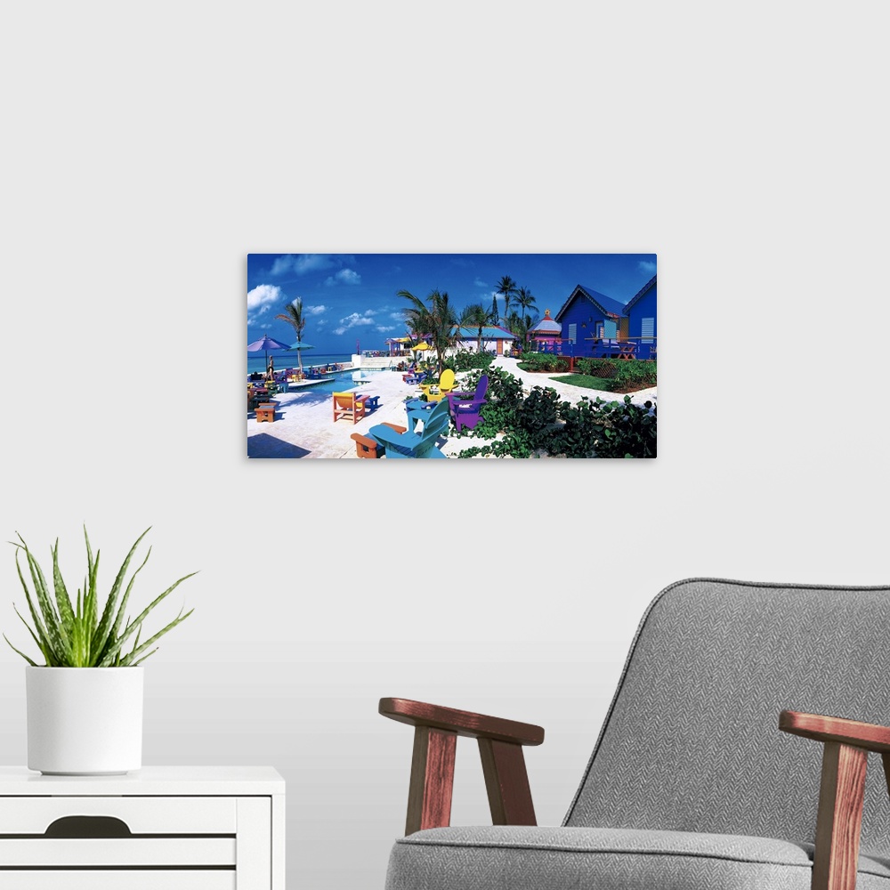 A modern room featuring Panoramic photograph of beachfront filled with beach chairs, umbrellas, beach goers, bungalows, a...