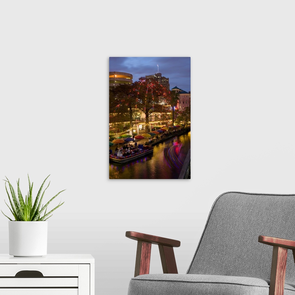 A modern room featuring Vertical photo on canvas of people eating at an outdoor restaurant next to a river underneath umb...