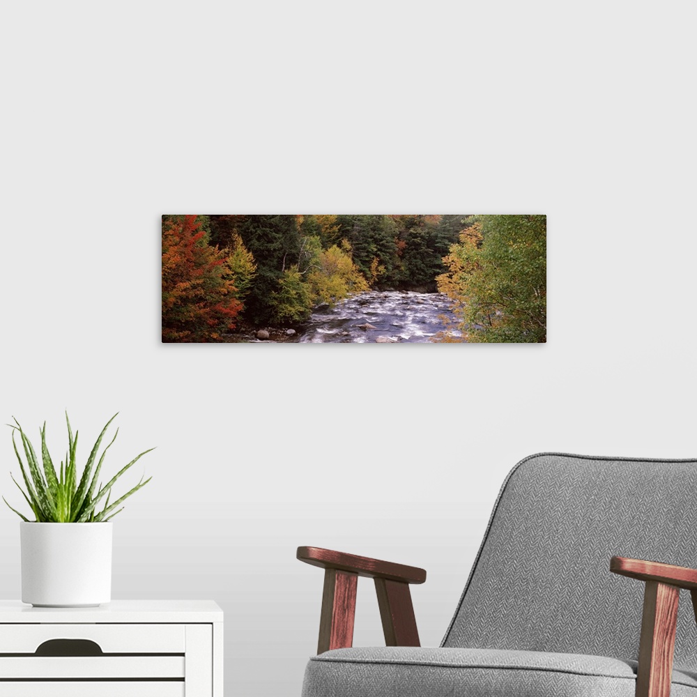 A modern room featuring This decorative landscape wall art is a panoramic photograph of a rock filled river riffling thro...