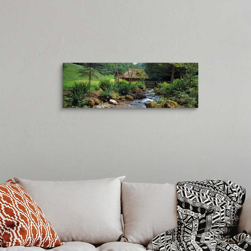 A bohemian room featuring Panoramic wall art of a bucolic scene in this photograph a river filled with moss covered boulder...