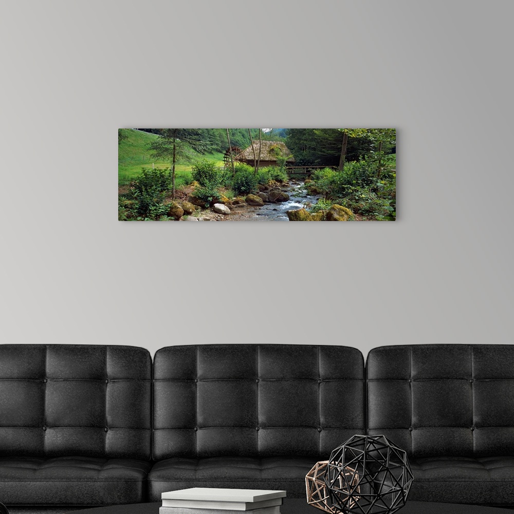 A modern room featuring Panoramic wall art of a bucolic scene in this photograph a river filled with moss covered boulder...