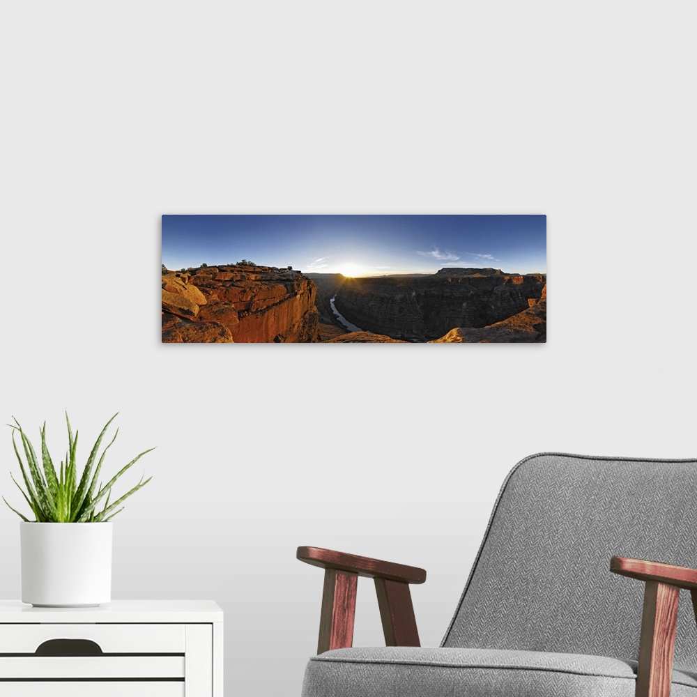 A modern room featuring A large panoramic photograph of the Grand Canyon with the river running through it and the sun se...