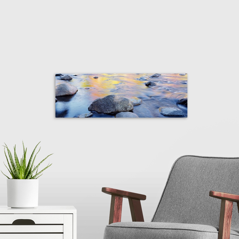 A modern room featuring Horizontal, big photograph of large rocks in a river, golden autumn colors reflecting in the wate...