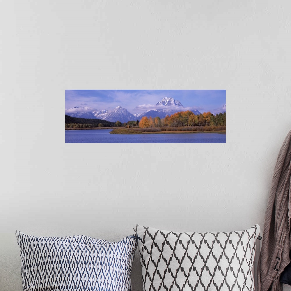 A bohemian room featuring Mountainous terrain with clouds hovering near the peaks is photographed from across a large body ...