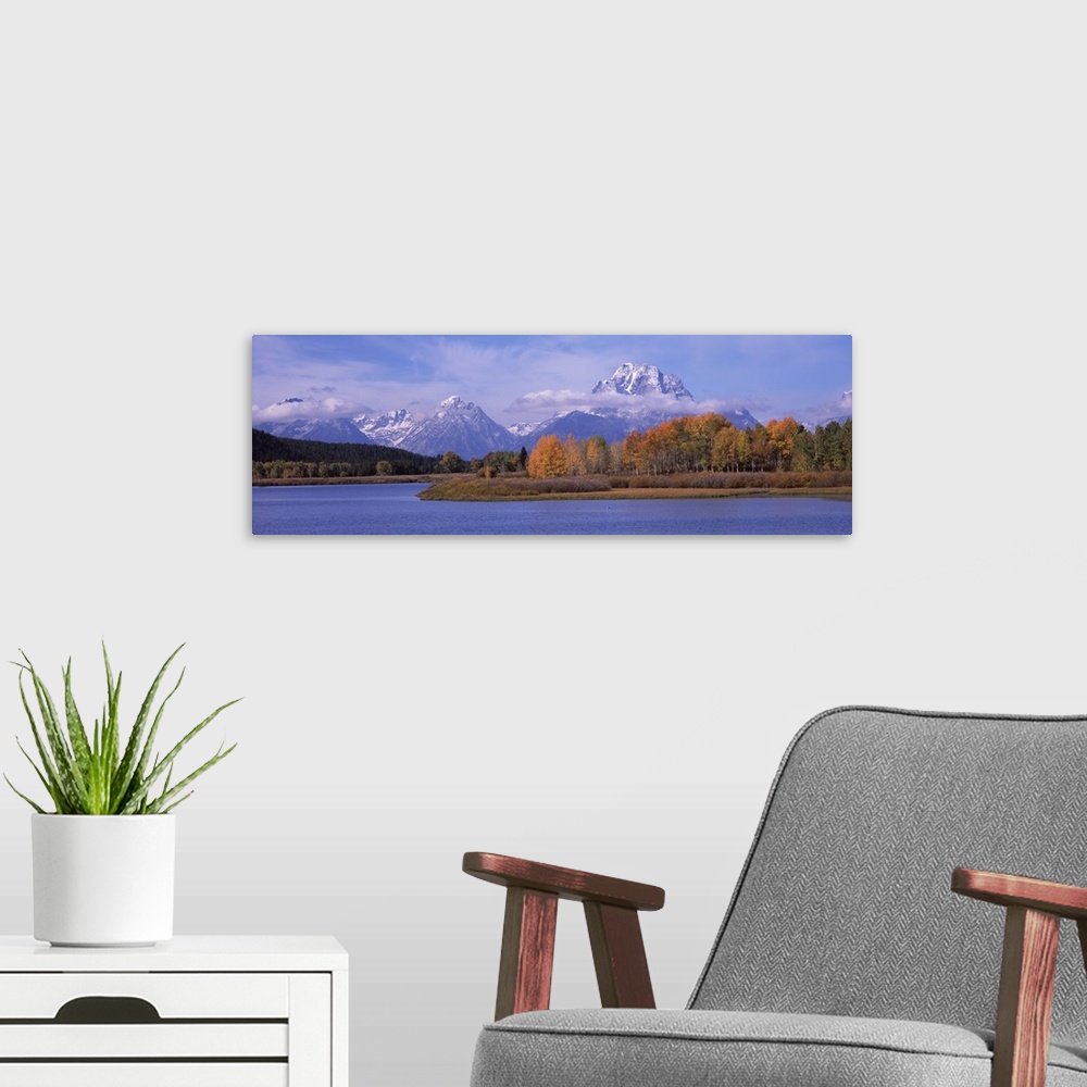 A modern room featuring Mountainous terrain with clouds hovering near the peaks is photographed from across a large body ...