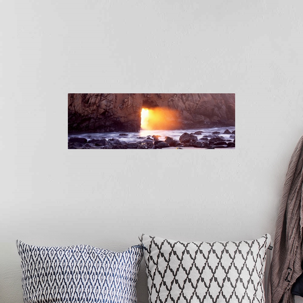 A bohemian room featuring Panoramic photograph of rocky shoreline with sun peering through huge stone arch-like structure.