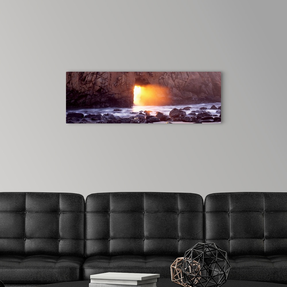 A modern room featuring Panoramic photograph of rocky shoreline with sun peering through huge stone arch-like structure.