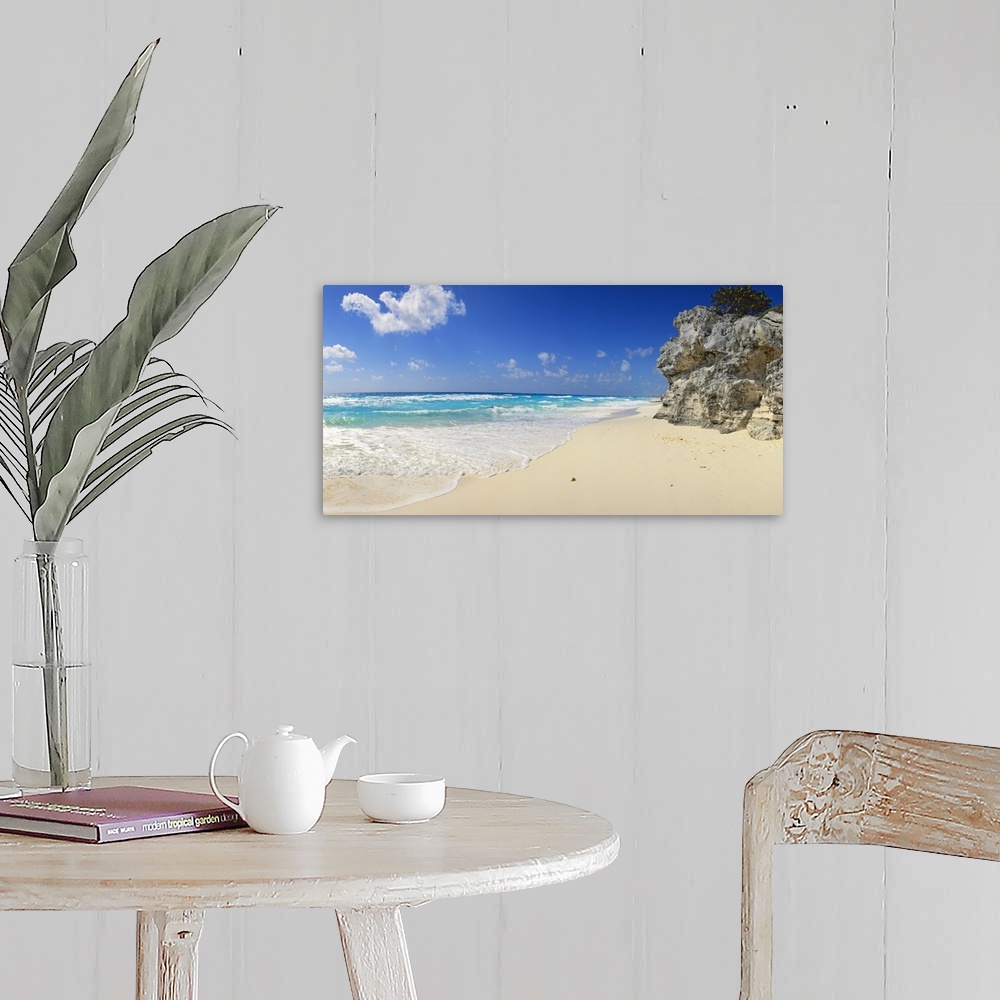 A farmhouse room featuring Panoramic photograph of beach with huge rock structure with tree on top.  Waves and sea foam and ...