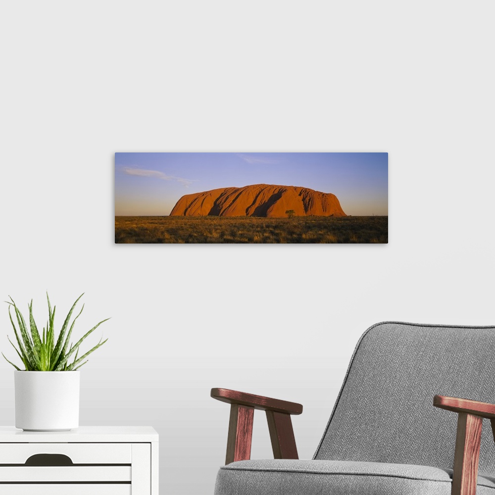 A modern room featuring A large sandstone landmark rises out of the desert plains in this panorama photographic wall art.