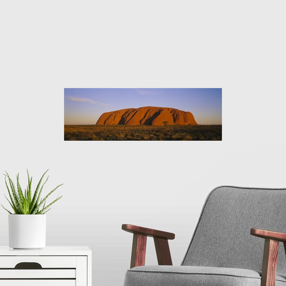 A modern room featuring A large sandstone landmark rises out of the desert plains in this panorama photographic wall art.