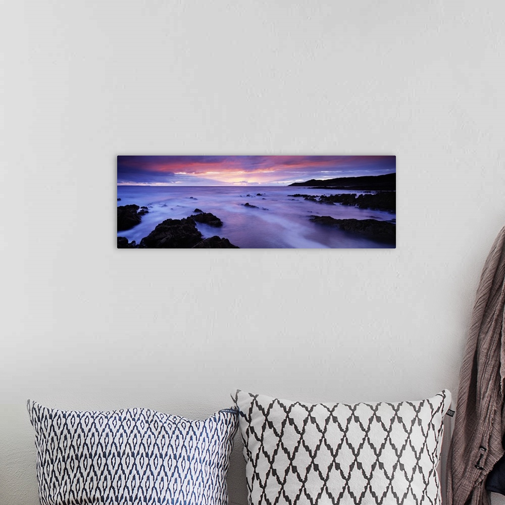 A bohemian room featuring Panoramic photo art of rock formations coming out of the ocean with a sunset in the distance.