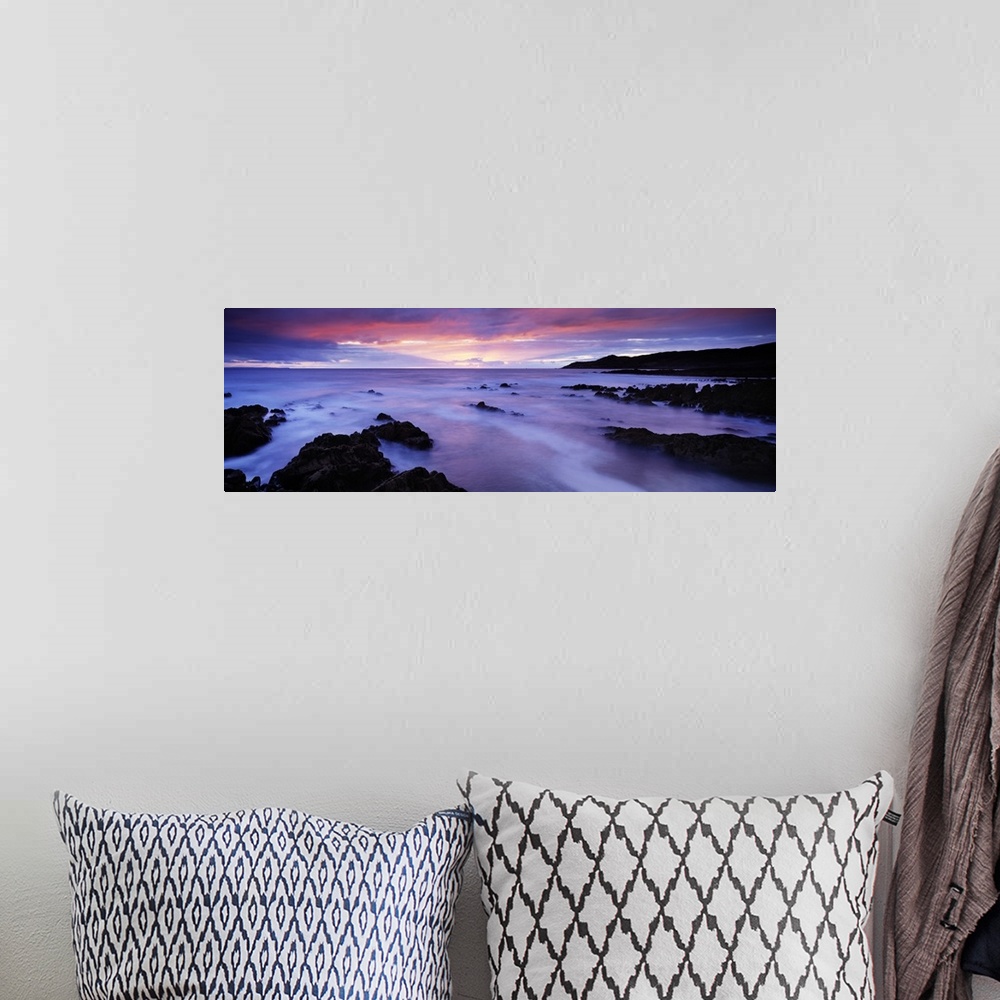 A bohemian room featuring Panoramic photo art of rock formations coming out of the ocean with a sunset in the distance.