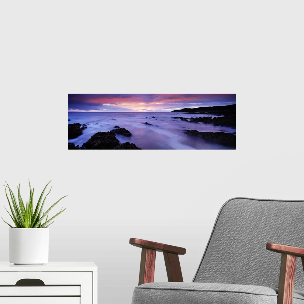 A modern room featuring Panoramic photo art of rock formations coming out of the ocean with a sunset in the distance.