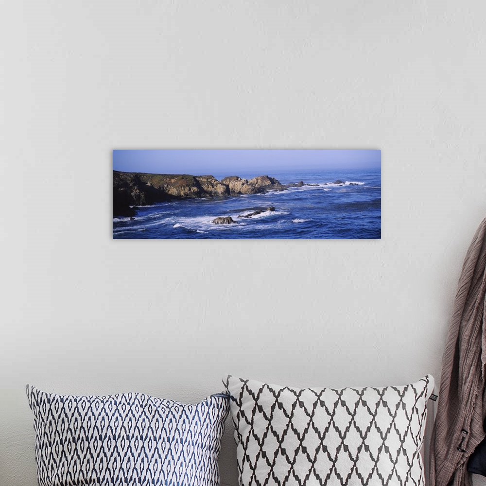 A bohemian room featuring Wide angle photograph of the bright blue waters of Big Sur lapping around large rock formations n...